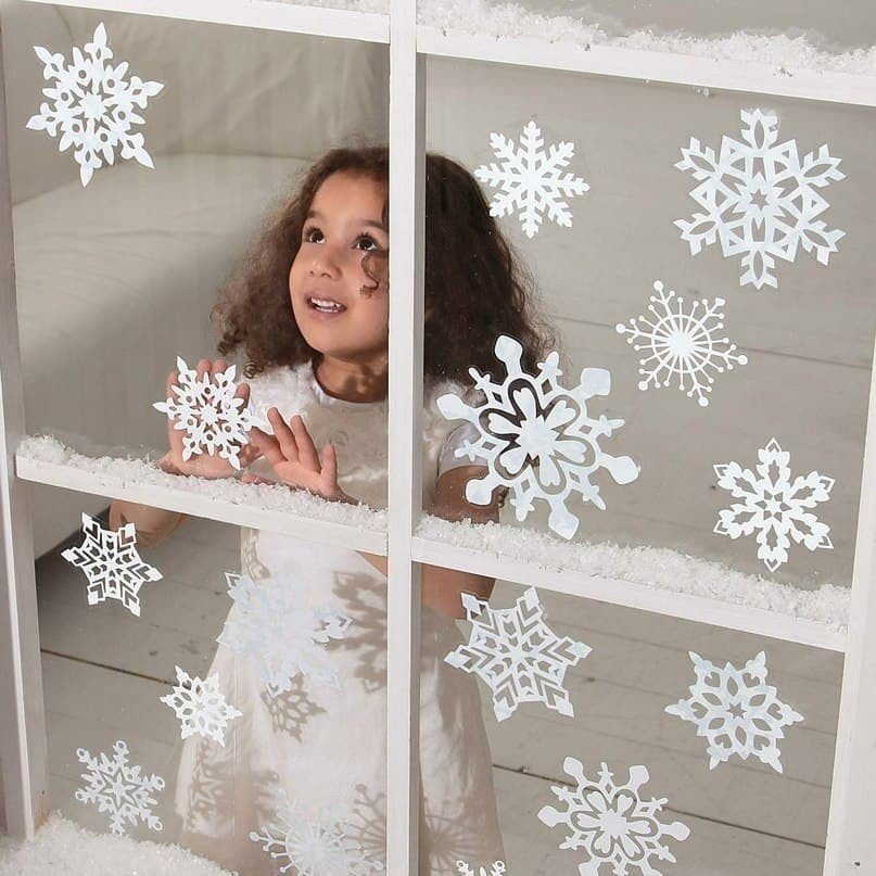 Девочка клеит снежинки на окно