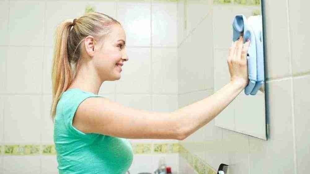 Женщина протирает зеркало
